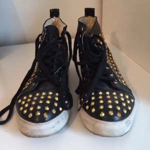  - Svarta sneakers med guldiga nitar från Nelly.