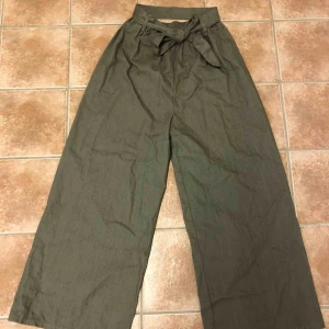  - Gröna byxor med utsvängda ben (bootcut) med snören i midjan som knyts där fram. HELT OANVÄNDA! Så dem är som nya! 