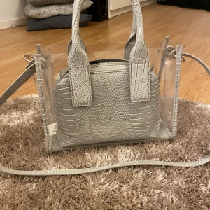 Väska från Zara - Transparant väska från zara i grå ormskinn detaljer (fake skinn). Necessär ingår till väskan men det går att ta ut den  man vill det. Möter upp i Halmstad eller fraktar (frakt 60kr). 