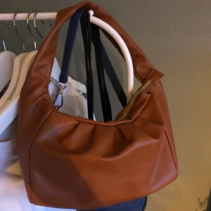 Axelväska  - Trendig axelväska i brun färg med guld tragkedja. Använd en gång.