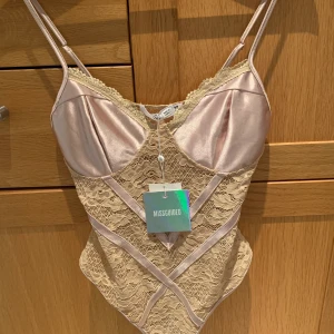Body - Hudfärgad satinbody med spets i storlek 38. Aldrig använd med prislappen kvar. Nypris: 303kr