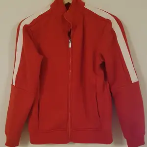 Röd sweatshirt jacka  med vita revärer på axlarna och en bit ner på ärmen. Använd men i bra skick. Passar perfekt på större S alt liten M
