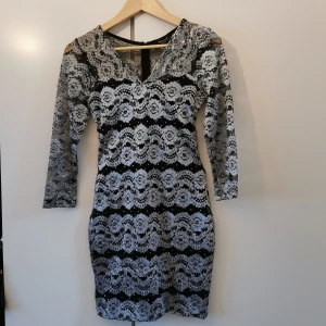 Glittrig klänning  - Perfekt nyårsklänning från SisterS point. Kort och figursydd klänning i silvrig spets och glitter. V-ringad och 3/4 ärmar. Storlek S, passar även XS. Dragkedja i bak. Använd endast ett fåtal gånger. 