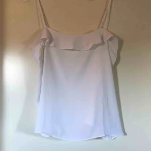  - Vitt, fint linne som passar till allt från H&M:s förra sommarkollektion. Volang upptill hela vägen runt både byst och rygg. Reglerbara axelband. Aldrig använd, prislapp är kvar. Strl 48, men lite mindre storlek. 100% polyester.