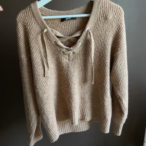 Stickad tröja - Brun/beige stickad tröja med snörning fram. Sparsamt använd. Super skönt material och sticks inte. Frakt tillkommer.