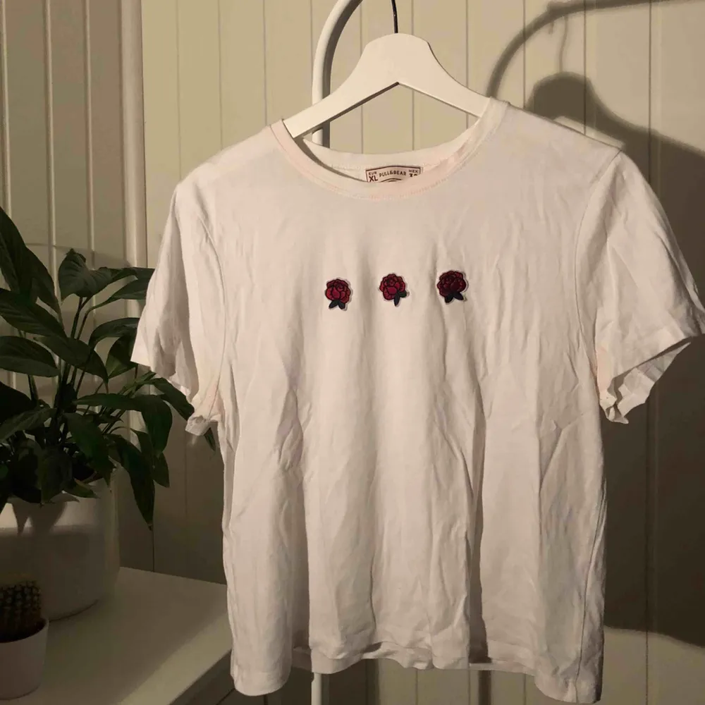 Super söt vit t-shirt med tre broderade rosor från Pull & Bear i väldigt bra skick! Står strl XL men sitter mer som en M (se sista bild för passform på mig som är S/M) Säljes pga används tyvärr inte längre 🌹   Fraktkostnad: 18 kr. T-shirts.