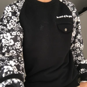 Sweatshirt Small - Svart sweatshirt med blommor på ärmarna och en ficka på bröstet