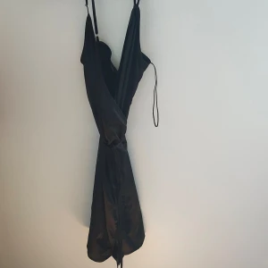 Svart NY klänning - Ny med lapp kvar från Zara. Svart klänning med glansigt material. Knyts i midjan. Ger en bra figur. 