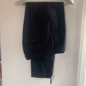  - Kritstrecksrandiga kostymbyxor i ullblandning. Bra skick, resår i midjan 