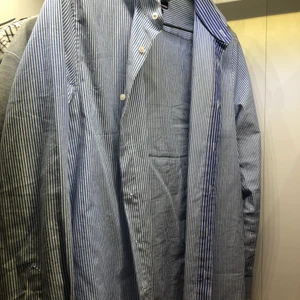 Blåvitrandig skjorta från Tommy Hilfiger - Snygg skjorta från Tommy Hilfiger. Perfekt till att ha en vit topp under till sommaren/våren eller bara som den är. Sitter oversized på mig som är en tjej med storleken M/S men normalt på en kille som är M/L.