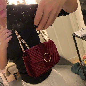Vinröd väska från Gina Tricot - En vinröd väska i sammet från Gina Tricot med gumddetaljer. Aldrig använd så i nyskick.