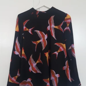 Skjorta med fåglar, M - Skjorta/blus i polyester. Dragkedja i ryggen som knäppning. Lös och skön passform. Storlek M, från BikBok Finns i stockholm, köpare står för frakt om det behövs.