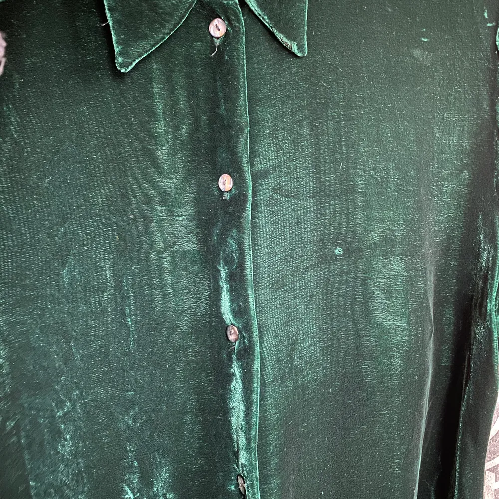Grön sammetsskjorta från Ebba Jensen i stl M. Av viskos och siden. Bra skick förutom ett litet hål fram på vänster sida (se bild 3). Kan postas mot 55kr porto.. Skjortor.