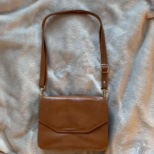Brun läderväska - En jätte praktiskt vintage handväska som har flera olika fack för förvaring i både fram-och baksida. Handväskan har även en spegel innuti och banden är justeringsbar. Väskan i sig är i väldigt bra skick. Frakt ingår inte i priset. Kan mötas upp i Stockholm söder.