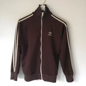  - Jättefin vintage Adidas-jacka i mörkbrunt med ränder och logga i off-white. Klassisk modell, passsar S-M. Väl använd men fint skick.  Kan posta eller mötas upp i Stockholm. 