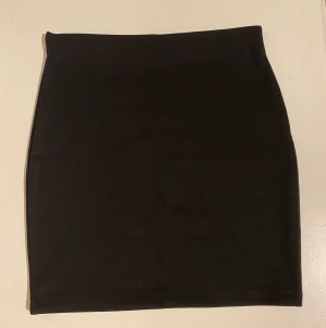 Tajt kort kjol - svart - Köpt för några år sedan, men endast använd ett fåtal gånger - superfint skick! Vet inte varför andra bilden ser glittrig ut, det är den inte. Svart vanlig kort kjol, perfekt basicplagg!! Resår i midjan, lite stretchig som formas efter kroppen 🤍 FRAKT INGÅR