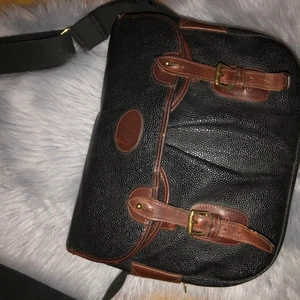 Mulberry trout bag - Mörkbrun/svart  med mörkbruna detaljer i läder. Beslag i gulfärgad metall. Två fack framtill. Insidan etikettmärkt "MULBERRY COMPANY MADE IN ENGLAND". På sidan plakett i metall: Med logo