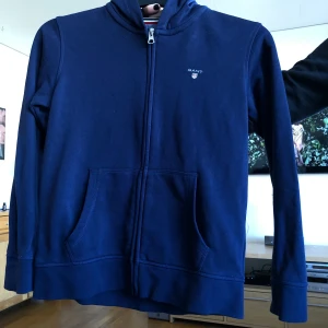 Gant - En mörkblå huvtröjor med dragskedja! Passar en liten XS eller 146/152. Aldrig använd förutom på bilden så det är väldigt bra skick! Originalpris är 699kr. Om du undrar något mer så är det bara att höra av dig! Frakten ingår inte i priset och betalas utav 