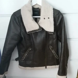 Brun läderjacka - Läcker bikerjacka / pilotjacka med invändig fluffigt tyg. Den har fler blixtlås och knappar samt funktionsdugliga fickor. Varm och mysig till hösten eller vintern! Inte använd av mig, alltså i nyskick!