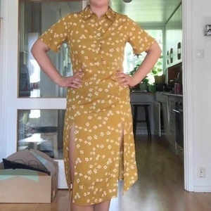 Blommig skjortklänning - Säljer denna gula skjortklänningen från asos. Den har knappar halva vägen och två slittar. Superfint skick då den aldrig är använd ❤