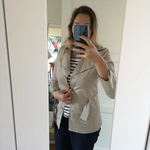  - Kort beige trenchcoat med stora knappar. 