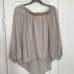  - Off-shoulder blus i glansigt beige material. 