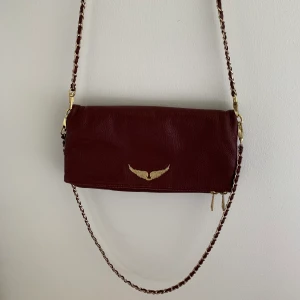 Zadig & Voltaire väska - Vinröd Zadig & Voltaire väska i läder med guld detaljer. Köpt för ca två år sedan på en outlet i USA. Den har tappat lite färg på baksidan, därav priset, men utöver det skulle jag säga att den är i bra skick. Du får med dustbag, två band (ett kortare och ett längre) och kvitto finns som äkthetsbevis!