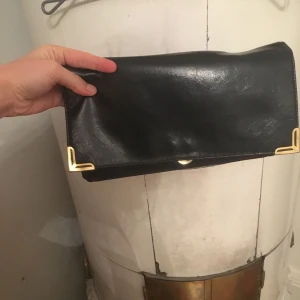  - Mörkblå/svart kuvertväska i skinnimitation m guldiga detaljer. Två stora fack + ett mindre m dragkedja