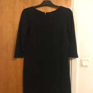  - Svart klänning i modellen ’Tinny’ från Vila. 3/4 ärm och guldig dragkedja baktill i nacken. Använd 1 eller 2 gånger så i mycket fint skick. Storlek S. 