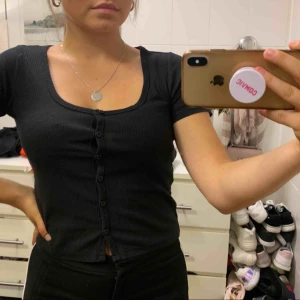  - Svart t-shirt med knappar. Lite kortare. Aldrig använd