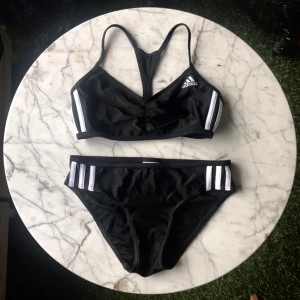  - Superfin bikini från Adidas med dom klassiska vita ränderna. Använd 1 gång tyvärr för liten för mig. Andra bilden visar baksidan på överdelen och den tredje bilden en detalj på baksidan av underdelen.  🖤☁️🖤☁️🖤 Kan mötas i Stockholm annars betalar köparen för portot 🌸