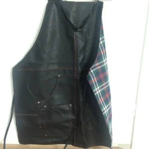  - Supersnyggt förkläde i äkta läder. Mjukt, rutigt tyg på insidan. Justerbart band runt nacken.  Säljer pga använder aldrig förkläde.