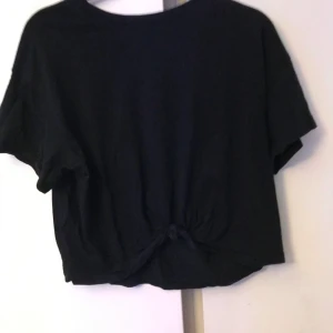 Svart T-shirt - Snygg svart från Bershka med snygg knytdetalj. Säljer för att den knappt är använd. Frakt tillkommer