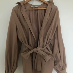 Skjorta NA-KD - Super fin oversized beige skjorta med knytning i midjan, skärpet får även att ta bort! Ballongärmar.  Använd endast ca 3 gånger. Storleken passar 34-40 skulle jag säga beror på hur man vill att den ska sitta då jag själv gillar att ha mina kläder oversized. 