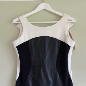 Kort klänning med skinndetalj - Söt festklänning med fejk skinndetalj på framsidan. Fick i julklapp och kom aldrig till användning, därav finns lappen kvar! Figursydd så väldigt snygg passform! Storlek S