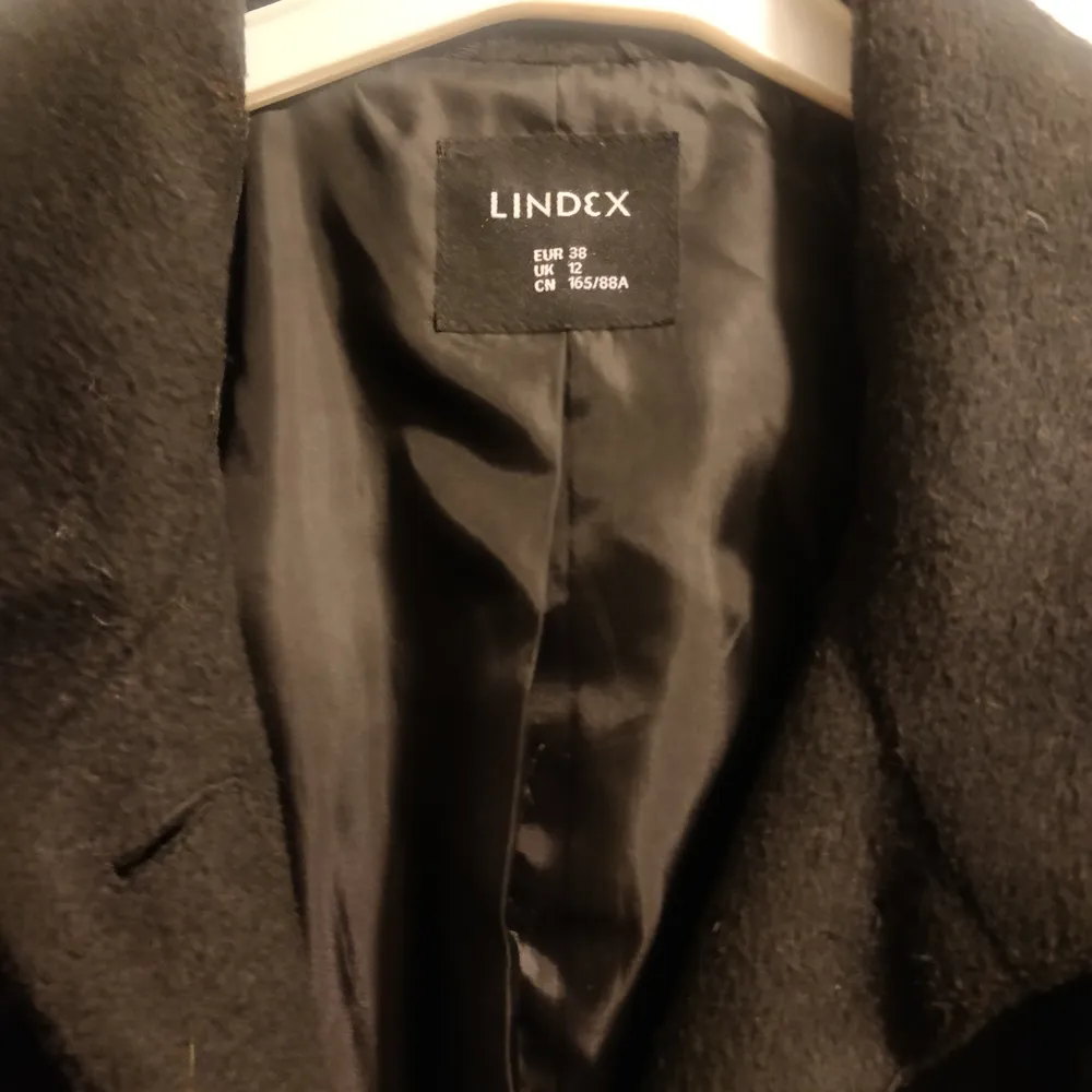 En svart ullkappa med skärp från Lindex i storlek 38. Köpt för 800 kr. 85% polyester, 15% ull. Jackor.