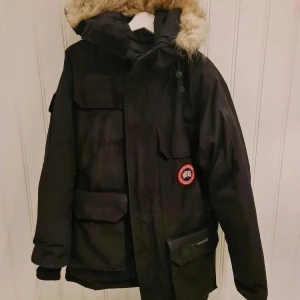 Canada Goose Jacka - Säljer min Canada Goose jacka i lång modell i färgen svart. Sparsamt använd. Den är lite blekt på fickorna där fram men annars är den i bra skick! Djur- och rökfritt hem. 