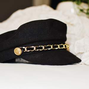 En svart hat/ keps med en guldkedja. Denna är ifrån Gina och har aldrig använt och därför jag säljer :) pris + frakt 