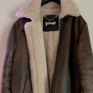 Aviatorjacka schott - Brun läderjacka med vitt sherpa-foder i lammull, långa ärmar, dragkedja, läderdragflik, två sidofickor i sidorna, tonstygnssöm, rak passform. Nypris: 9500kr. Jackan är liten i storlek passar L-XL. Finns att hämta i Sundbyberg. Kan skickas, köparen betalar frakt.