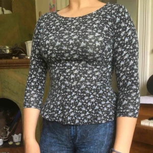  - Peplumtop, trekvartslång tight ärm. Mörkblå botten, blommönster, små ljusblå och vita blommor.