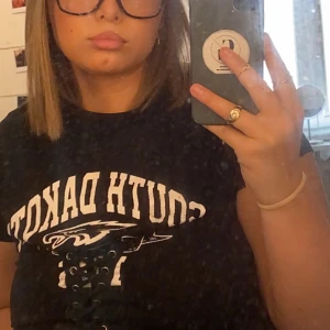 T-shirt - Svart t-shirt med snörning över brösten/ magen. Kommer inte till användning längre. Storlek xs men jag är själv M och passar mig bra. 150kr frakten ingår i priset!