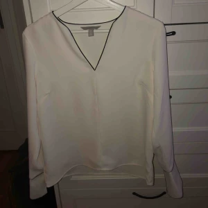  - Vit blus med svarta detaljer vid halsen och ärmarna, även som slits på ärmarna, jättefint att vika upp de. Använd några få gånger och i bra skick. Frakt 50kr, pris kan diskuteras.