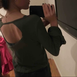  - En militärgrön ribbad tröja med utsvängda armar som också är öppen i ryggen. 