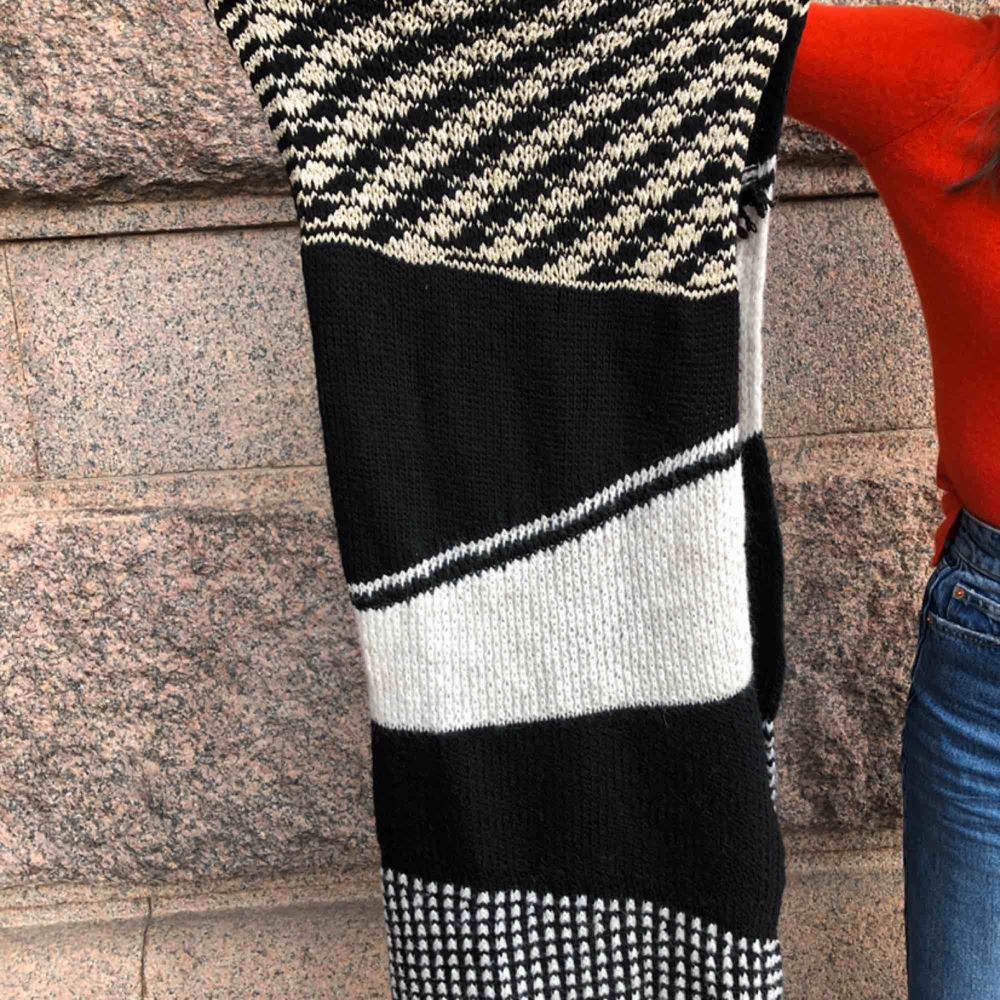 Knitted stretchy long scarf. White and black with gold accent. Stickat.