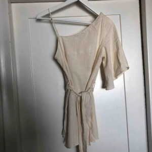  - Längre topp i off-whitelinnetyg, asymmetrisk med en bar axel och band som kan knytas i midjan. Korta slitsar på sidorna från Zara.  Använd en gång.  Kan mötas upp eller frakt för 30kr.😊