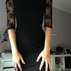 Svart festklänning  - Aldrig använd svart klänning med spets armar, off shoulder och en detalj vid bröstet, se andra bilden. Lite mörka bilder så fråga gärna om fler om ni vill se. Nypris 300:-. Mitt pris 80 kr inkl frakt