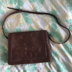 Brun väska - Stor brun väska i italienskt läder! Tre stora och två små fack. Väldigt rymlig och mjuk. Väskan är 28 x 22 cm. Axelbandet är justerbart, när det är som längst är det 1 meter, alltså ganska kort.