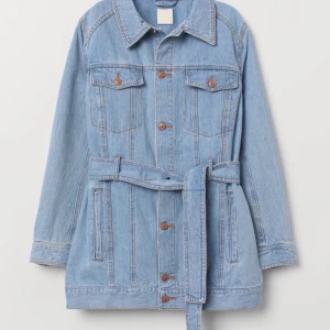  Jeansjacka strl 40 -  Lång jeansjacka med knytskärp, bra skick.                       Möts upp i Sthlm annars står köparen för frakt.