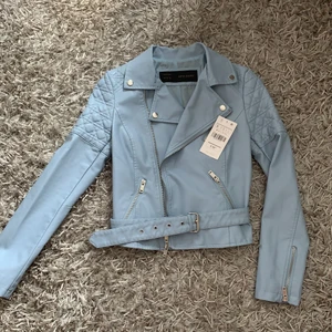 Babyblue skinnjacka  - Helt ny och oanvänd skinnjacka (veganskt skinn) i en fin ljusblå färg. Passar utmärkt till vår/sommar över en croptop topp och ett par jeansshorts. Fina quiltade detaljer vid axlarna samt avtagbart bälte. Frakt ingår. Avhämtning hos mig i Solna. 
