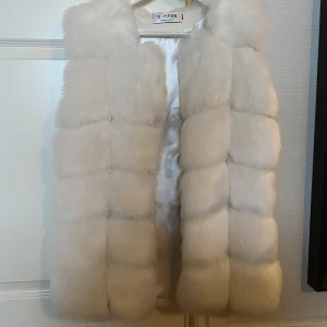 Vit fuskpälsväst  - Vit fuskpälsväst i storlek M, har hakar på insidan så man kan stänga den, använd Max tre gånger, är 173 och har vanligtvis S/M